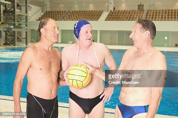 three senior men wearing swimwear, holding football at poolside - old man in speedo stockfoto's en -beelden