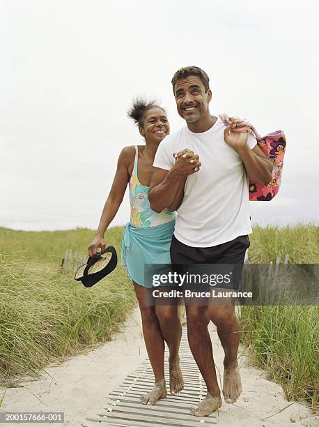 mature couple walking on boardwalk, holding hands - beach black and white stock pictures, royalty-free photos & images