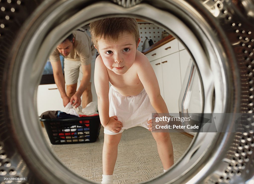 Young boy (4-6) looking inside washing machine,  father in background