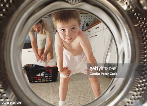 young boy (4-6) looking inside washing machine,  father in background - family looking at camera stock pictures, royalty-free photos & images