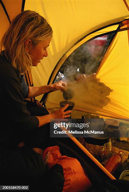 female camper brewing tea in tent, side view - travel12 stock pictures, royalty-free photos & images