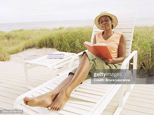 mature woman reading book in lounge chair near beach - beach book reading stock-fotos und bilder