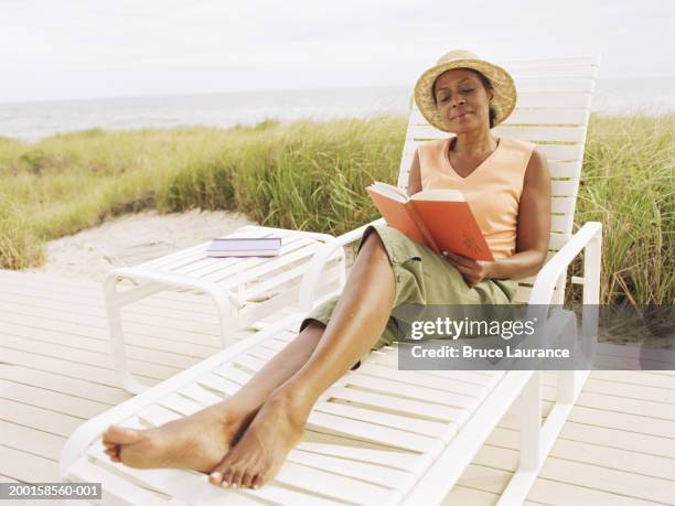 mature woman reading book in lounge chair near beach - beach book reading stockfoto's en -beelden