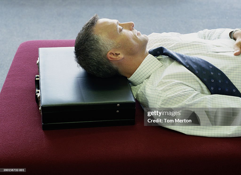 Business man lying down with head resting on briefcase, eyes closed