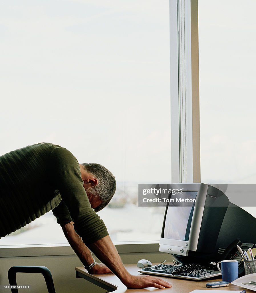 Mature man leaning on office desk, side view