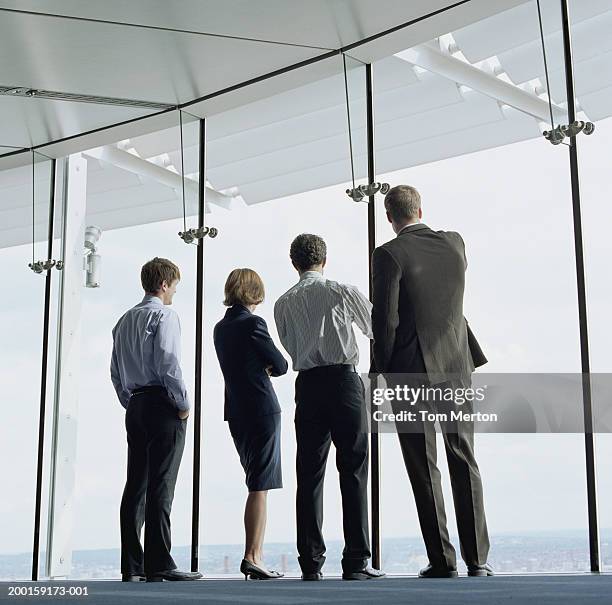 four business colleagues looking out of office window, rear view - bussines group suit tie stock-fotos und bilder