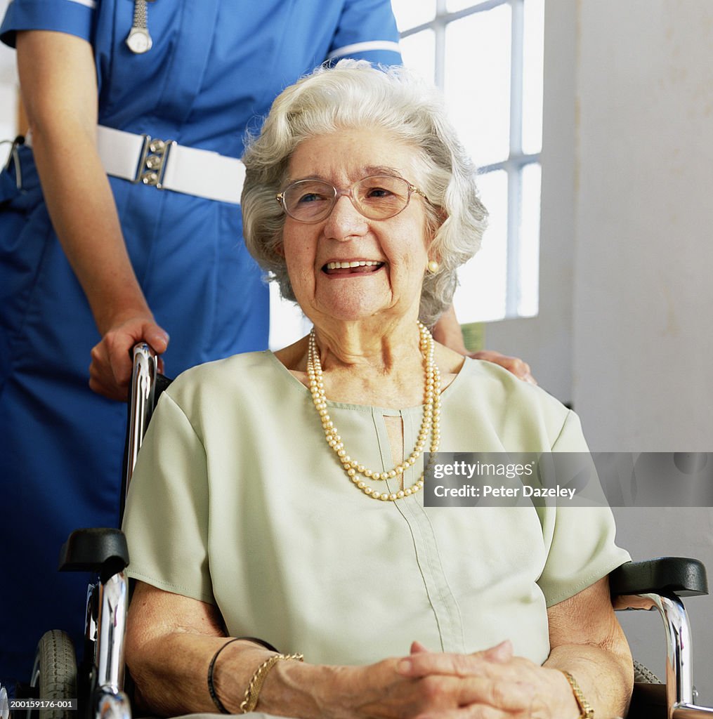 Senior woman in wheelchair being pushed by nurse, smiling