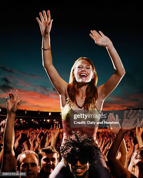 woman sitting on man's shoulders amongst crowd at concert, sunset - concierto de música pop rock fotografías e imágenes de stock