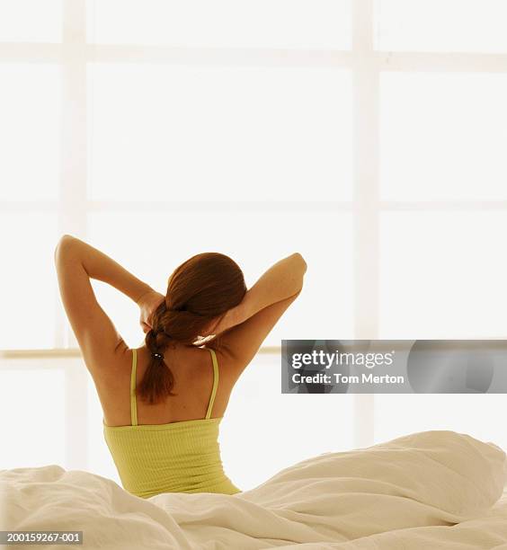 woman sitting on bed, stretching arms, rear view - キャミソール ストックフォトと画像