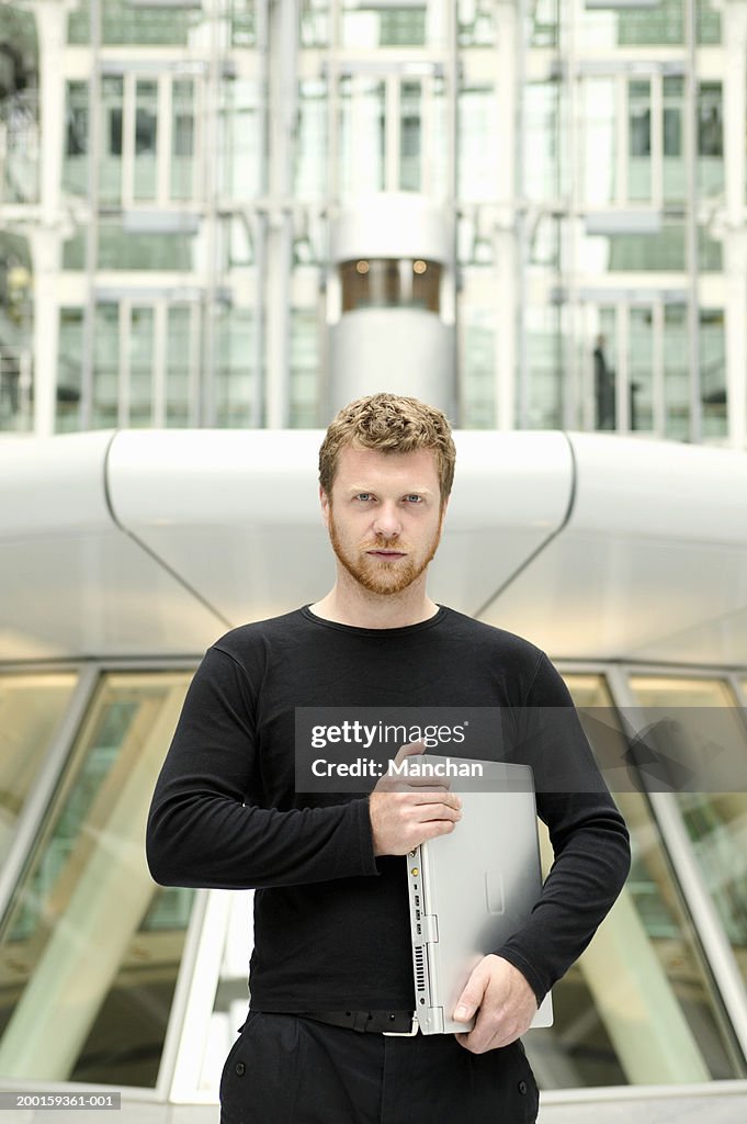 Young man holding laptop computer, portrait