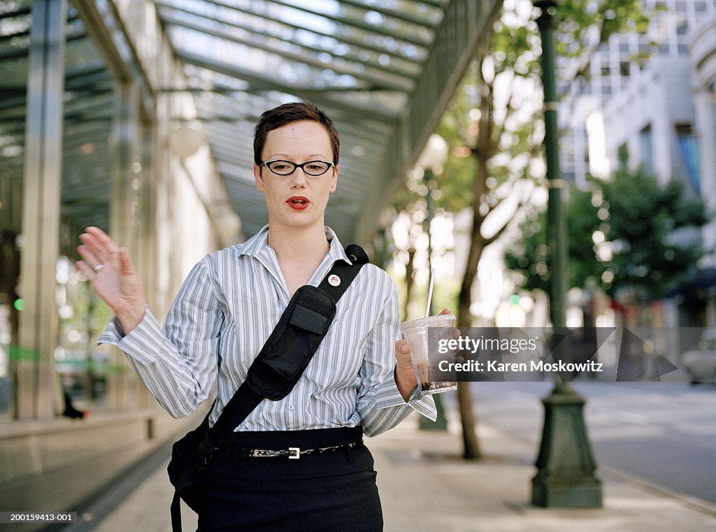 Woman walking on urban sidewalk, carrying coffee drink