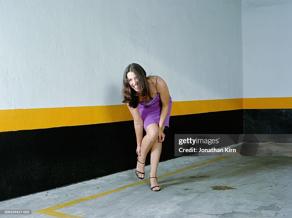 Woman adjusting shoes in empty parking lot, smiling