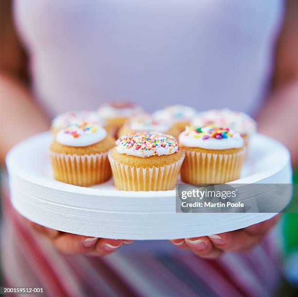 woman carrying cakes on pile of paper plates, mid section, close-up - cupcake foto e immagini stock
