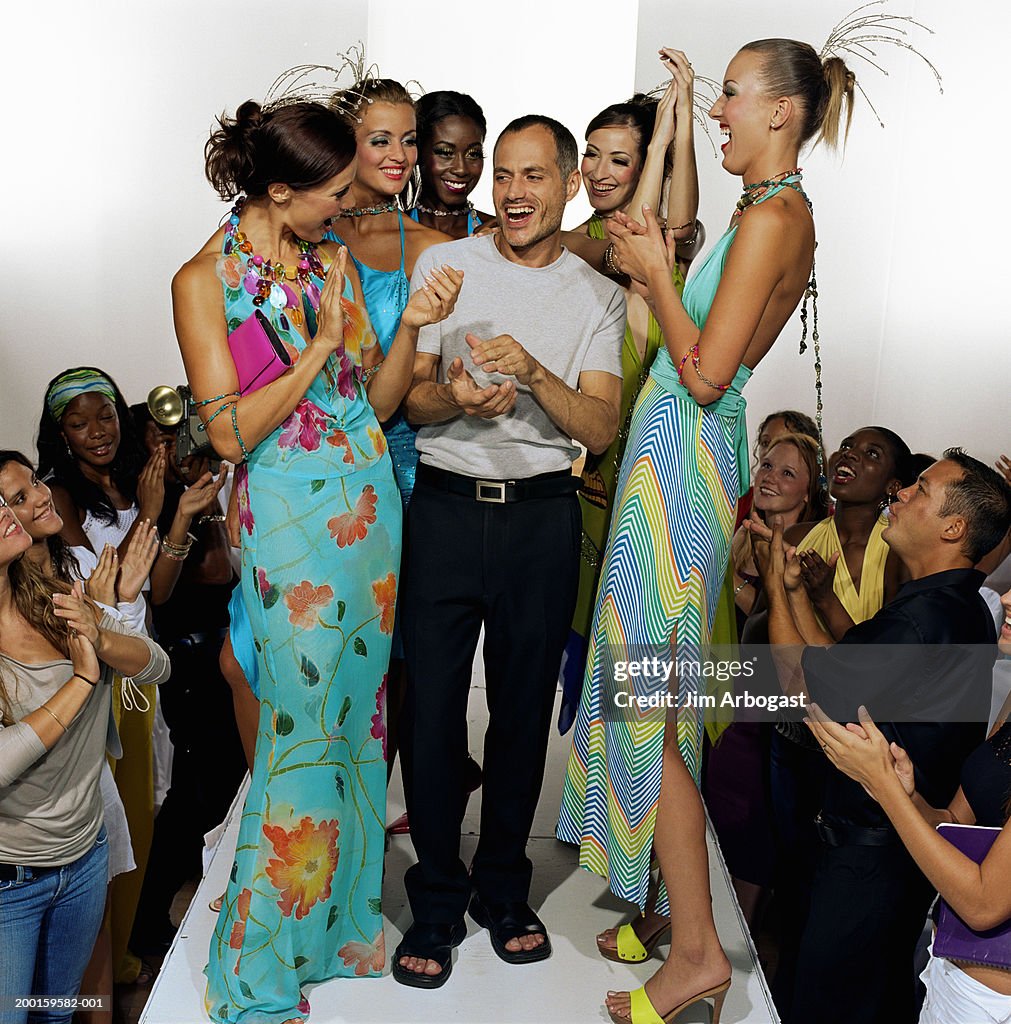 Models surrounding fashion designer on catwalk after fashion show