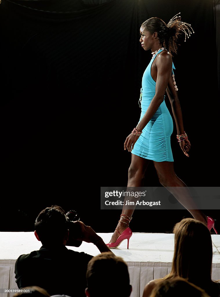 Fashion model walking on catwalk during fashion show, side view