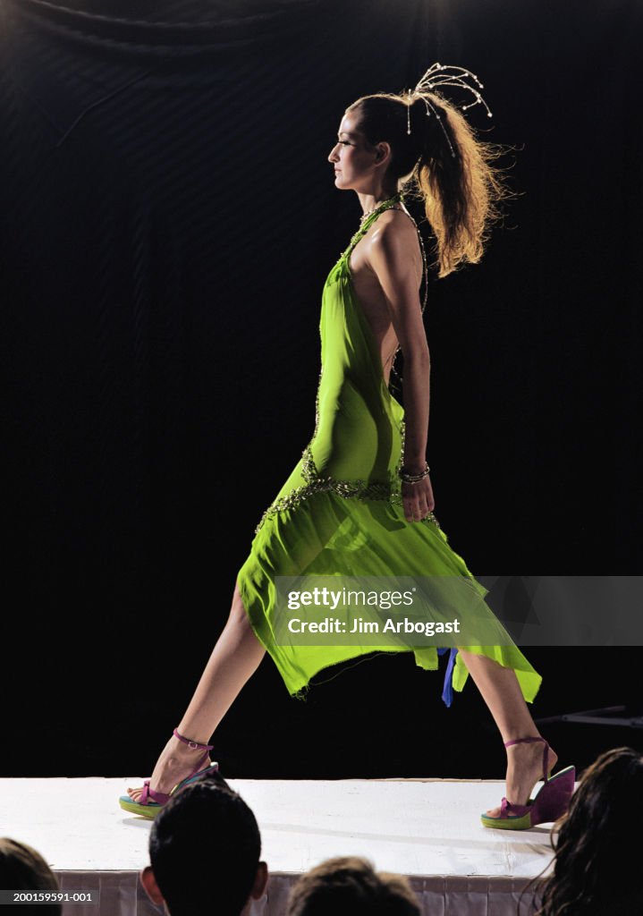 Fashion model walking on catwalk during fashion show, side view