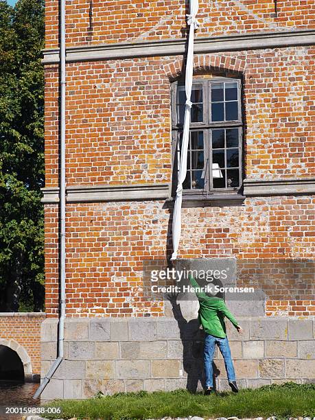 man reaching for knotted sheets hanging from building, rear view - bettbezug stock-fotos und bilder