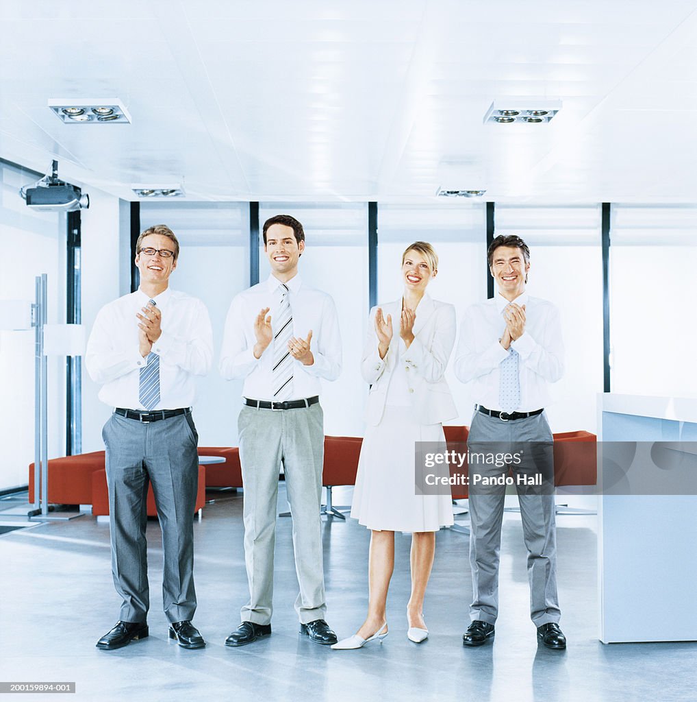 Four business colleagues applauding in office, portrait