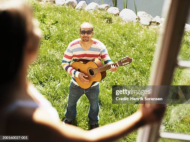 man serenading woman at window (focus on man playing guitar) - cantare una serenata foto e immagini stock