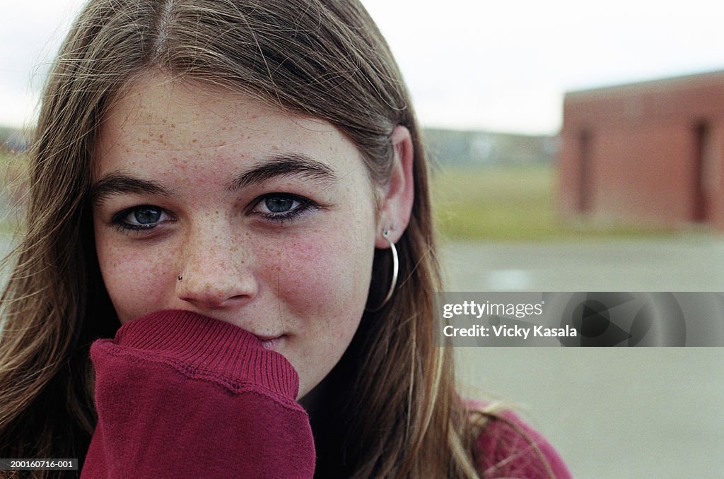 Teenage girl (13-15) covering mouth with sweatshirt sleeve
