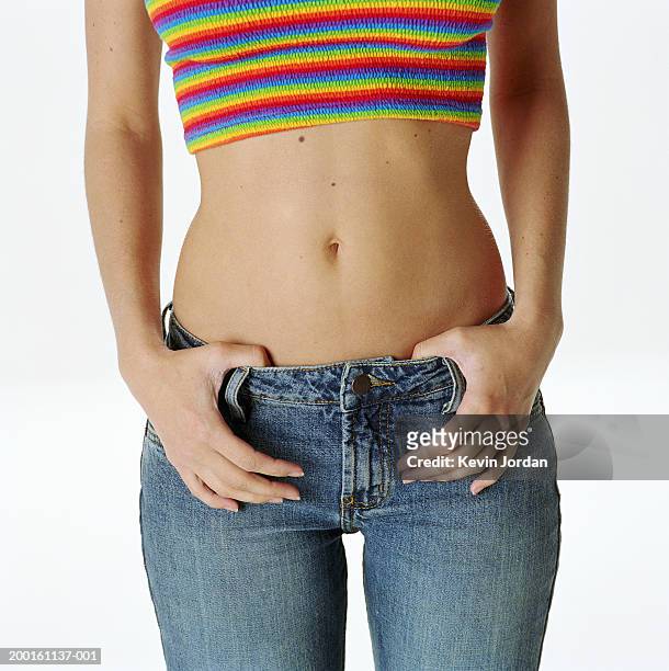 young woman with thumbs hooked in jean's waist band, mid section - pantalón de cintura baja fotografías e imágenes de stock