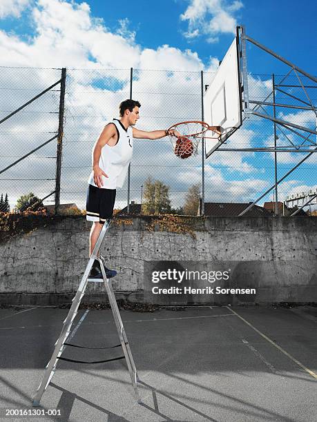 young man on step ladder, dunking basketball in hoop, side view - facilité photos et images de collection