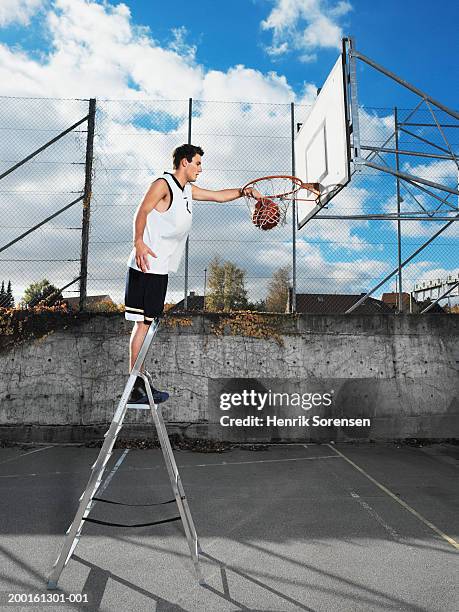young man on step ladder, dunking basketball in hoop, side view - commode photos et images de collection