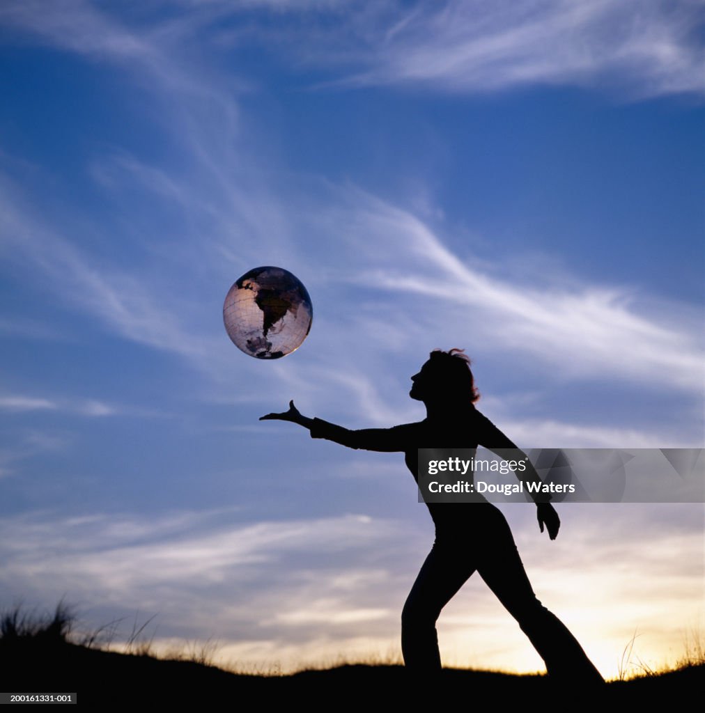 Young woman outdoors at sunset with inflatable globe, silhouette