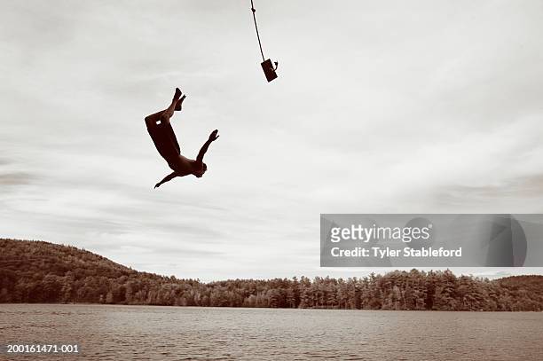 young man jumping into lake from rope swing (digital enhancement) - altalena di corda foto e immagini stock