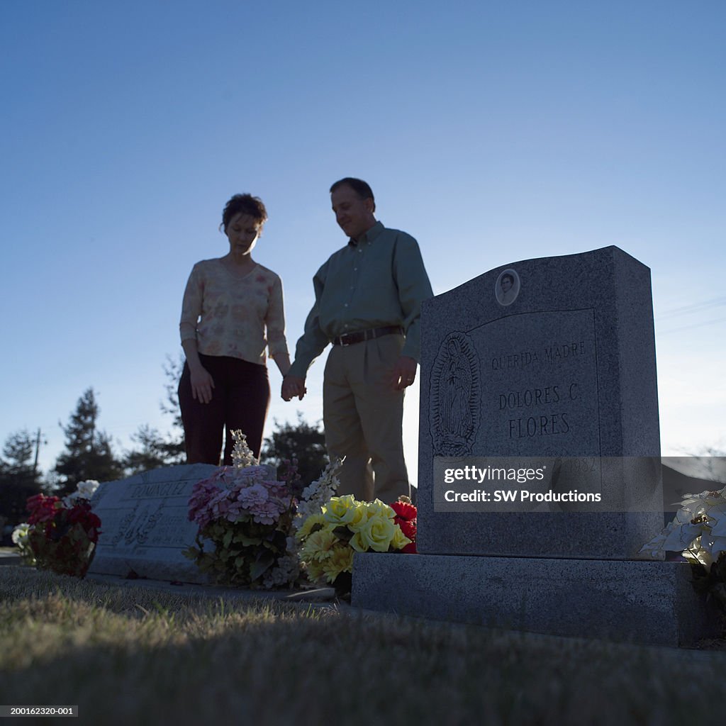 Man and woman holding hands in cemetery (focus on tombstone)