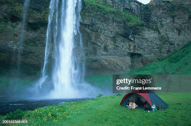 woman lying in tent reading book, waterfall in background - travel12 stock pictures, royalty-free photos & images