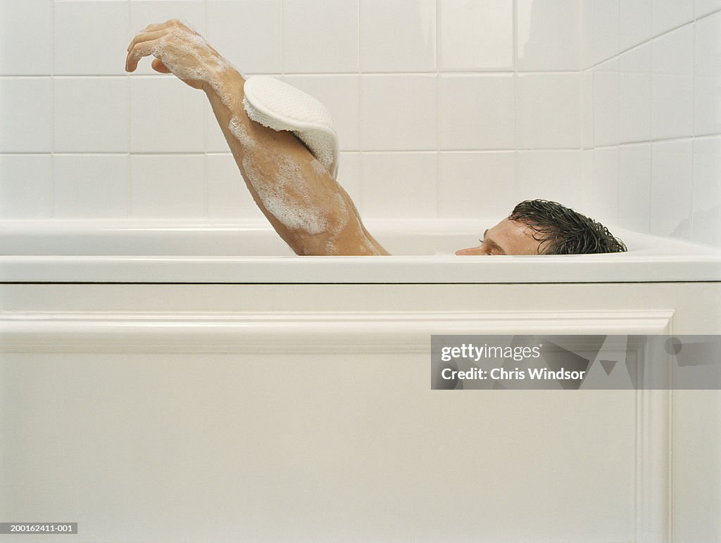 Man in bath using loofah mitten on arm, side view