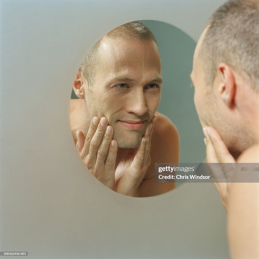 Man with hands on face, looking at reflection in mirror