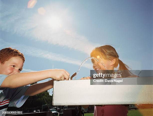 boy and girl (5-7) using water fountain in park - drinking fountain stock pictures, royalty-free photos & images