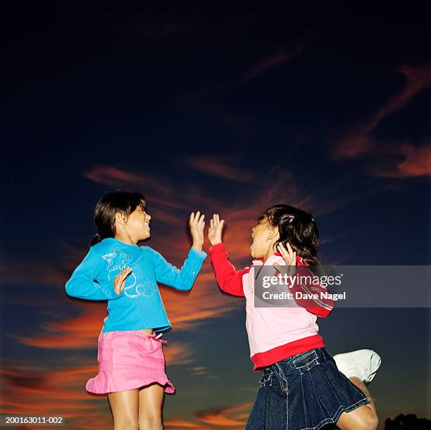 two girls (5-7) jumping, slapping hands - stoneplus8 stock pictures, royalty-free photos & images