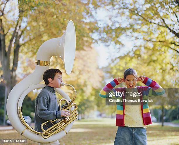 girl (8-10) standing beside boy (8-10) playing tuba, plugging ears - vingers in de oren stockfoto's en -beelden