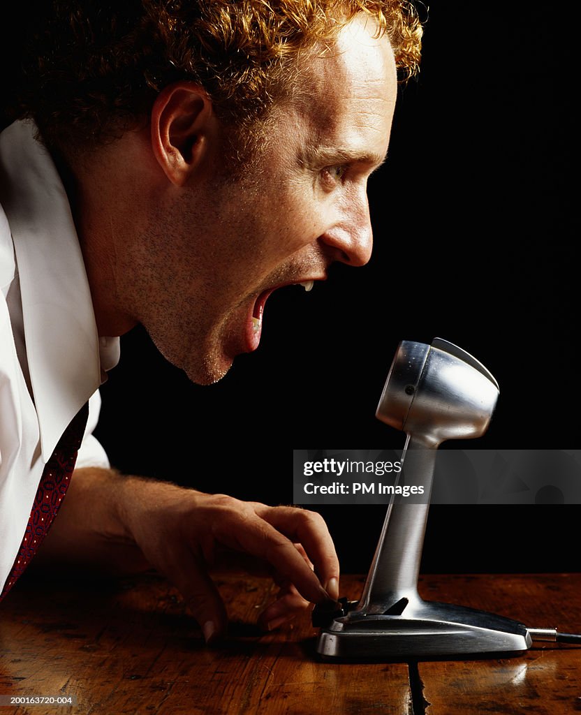 Businessman shouting into microphone, profile, close-up