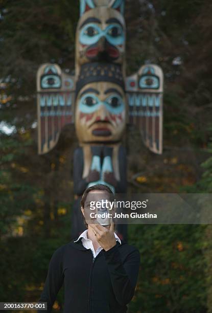 woman using digital camera in front of totem pole (focus on woman) - revillagigedo island alaska stockfoto's en -beelden