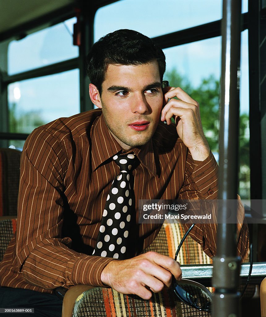 Young businessman sitting on bus, using mobile phone