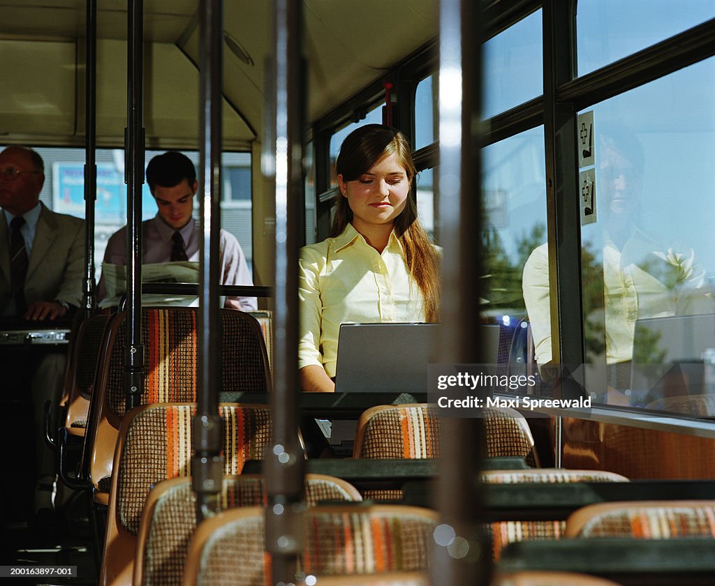 Young businesswoman sitting on bus, using laptop