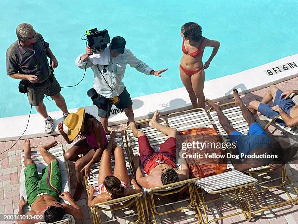 group of adults lying by poolside, film crew giving instructions - telerrealidad fotografías e imágenes de stock