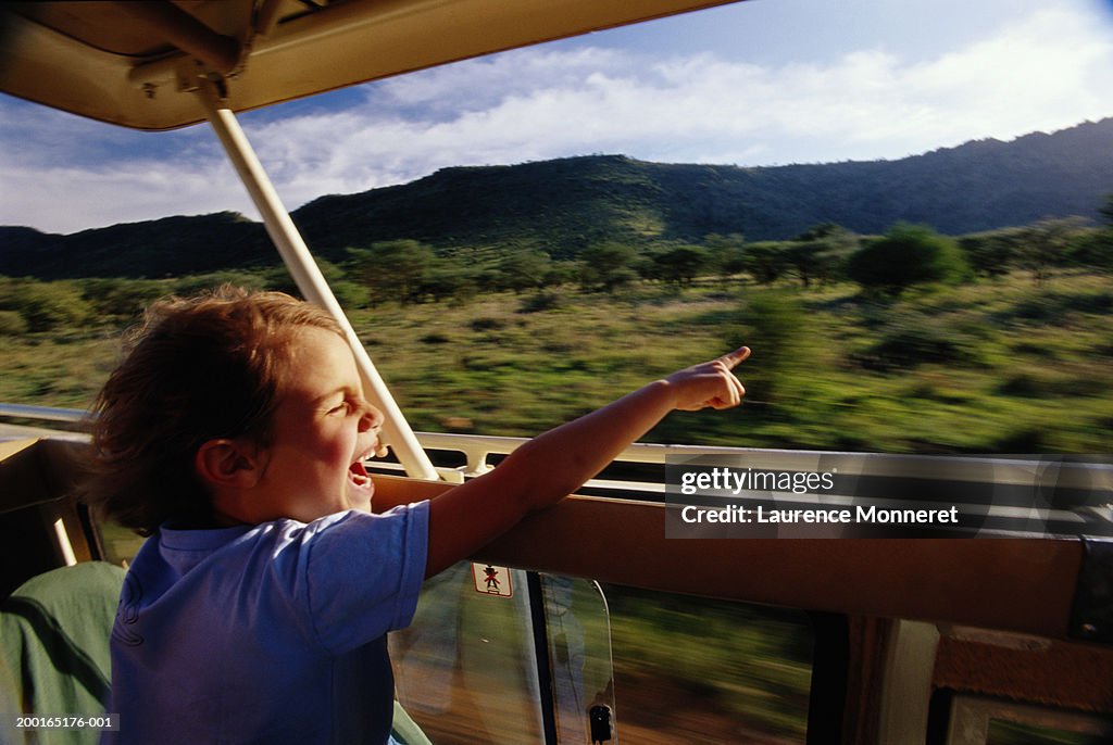 Boy (5-7) sitting in safari vehicle, pointing (blurred motion)