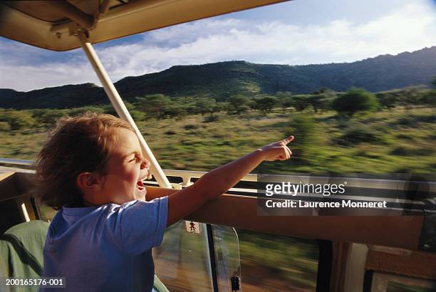 boy (5-7) sitting in safari vehicle, pointing (blurred motion) - classic car point of view stockfoto's en -beelden
