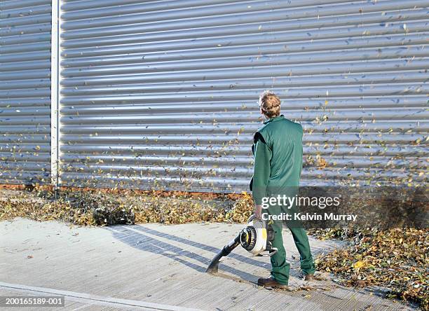man clearing leaves with leaf blower, rear view - leaf blower stock pictures, royalty-free photos & images