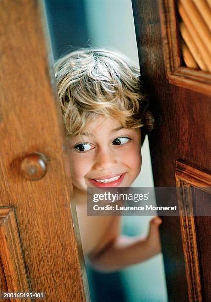 boy (5-7) peering through doorway, smiling, close-up - door ajar stock pictures, royalty-free photos & images