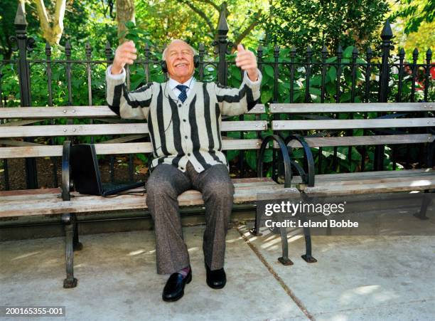 senior man listening to music from laptop, gesticulating in park - musical conductor stock pictures, royalty-free photos & images