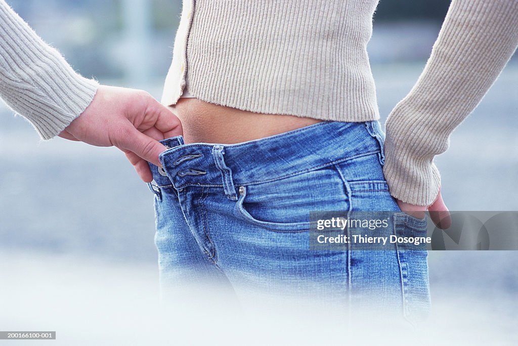 Man pulling on woman's jeans, mid section
