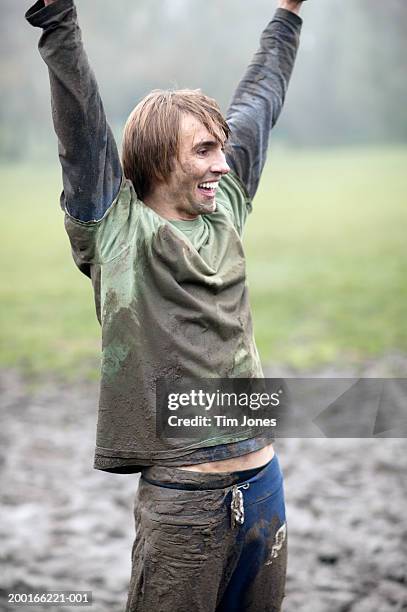 young man standing on muddy field, arms raised, smiling - アマチュア選手 ストックフォトと画像