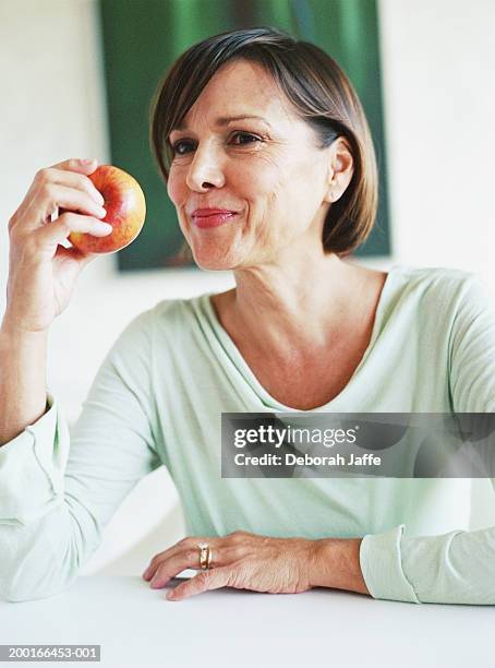 mature woman holding apple, smiling - frau apfel stock-fotos und bilder