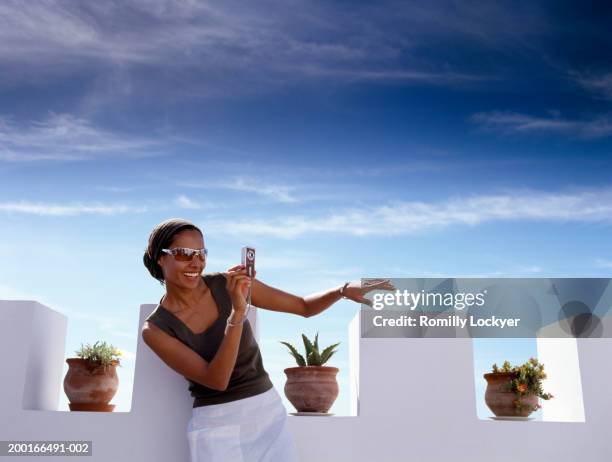 young woman taking photograph, on roof terrace, smiling, mid section - travel12 stock pictures, royalty-free photos & images